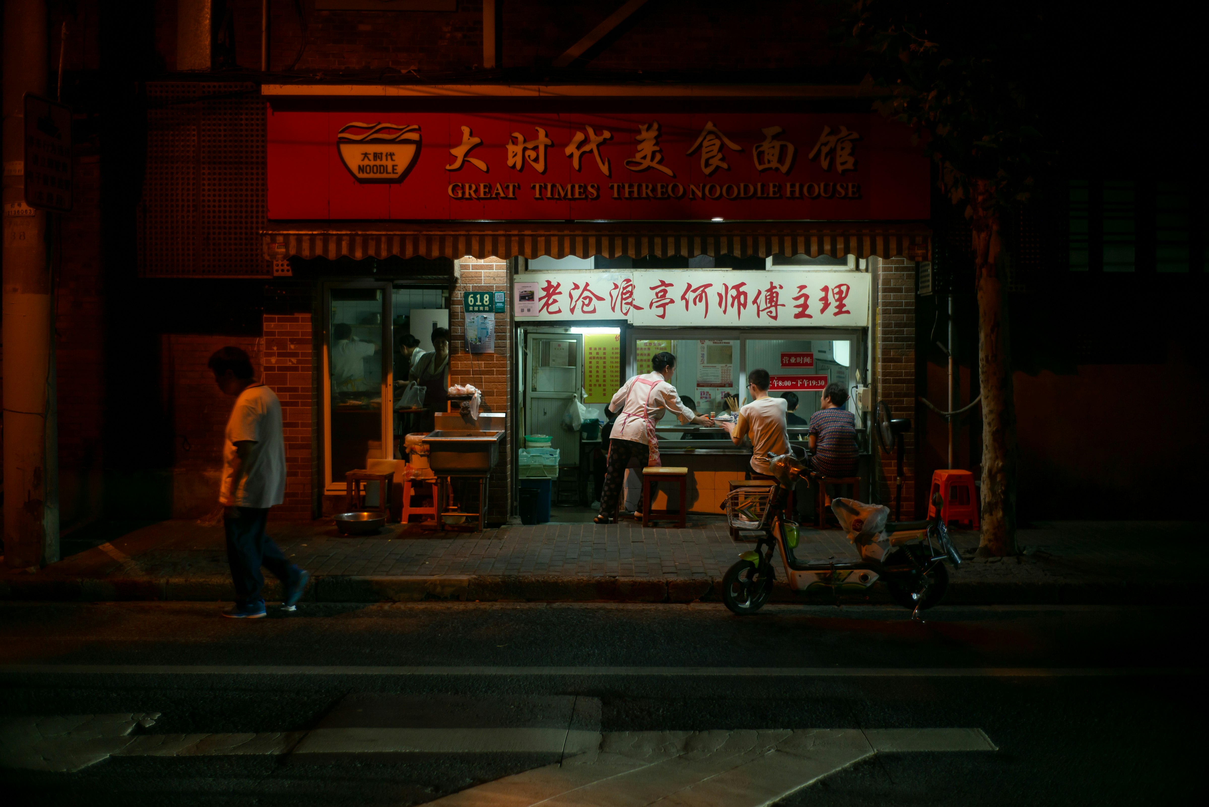 man in white t-shirt and black pants standing near store during night time